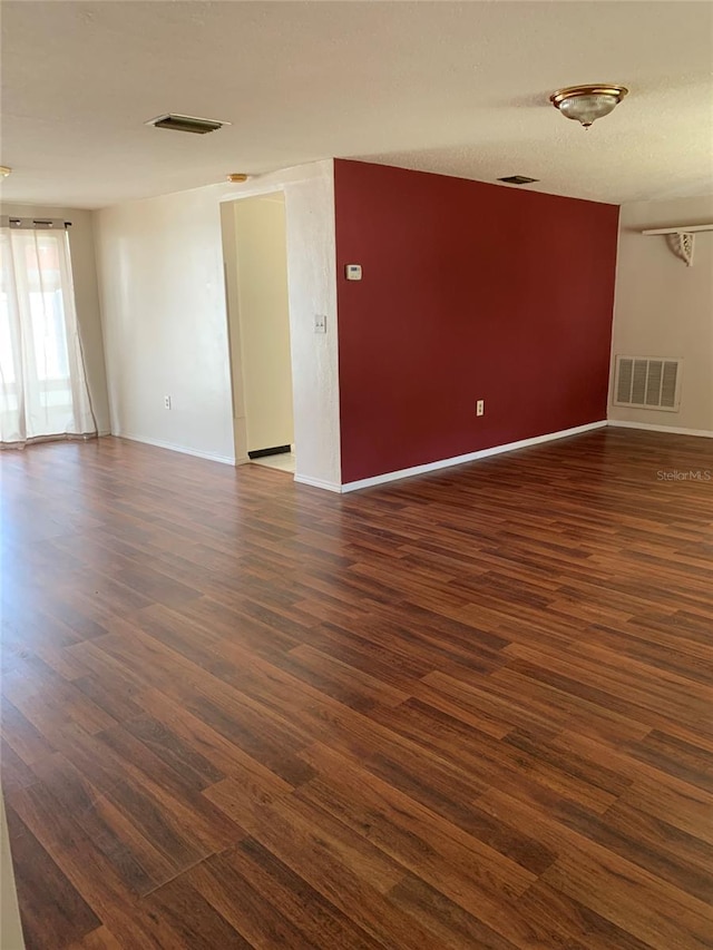 spare room featuring a textured ceiling, dark wood-style floors, visible vents, and baseboards