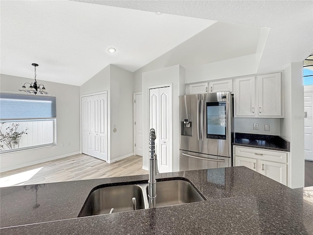 kitchen with white cabinets, decorative light fixtures, vaulted ceiling, stainless steel refrigerator with ice dispenser, and a sink