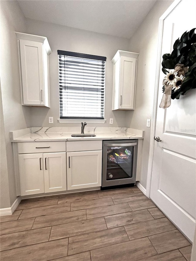 bar with beverage cooler, baseboards, a sink, and wood finish floors