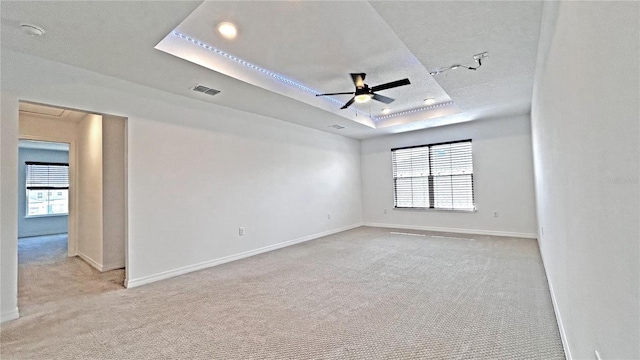 spare room with visible vents, a tray ceiling, a wealth of natural light, and light colored carpet