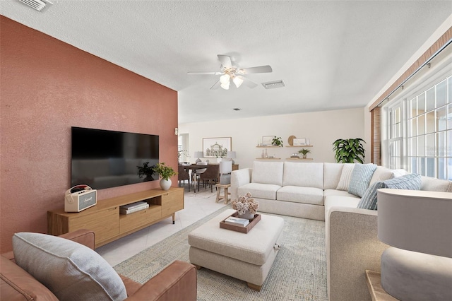 living room with a ceiling fan, visible vents, a textured wall, and a textured ceiling