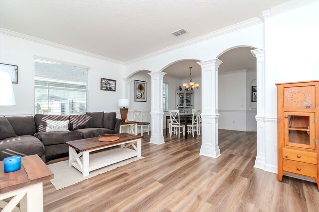 living room featuring hardwood / wood-style flooring, crown molding, decorative columns, and an inviting chandelier