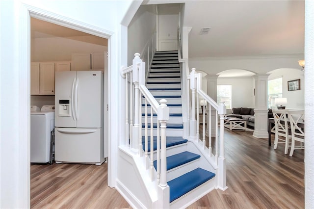 staircase featuring hardwood / wood-style flooring, ornamental molding, ornate columns, and independent washer and dryer
