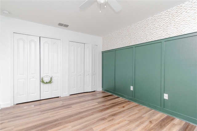 unfurnished bedroom featuring ceiling fan, two closets, and light wood-type flooring