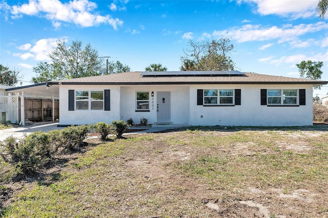 ranch-style home with a front yard, fence, roof mounted solar panels, a carport, and stucco siding