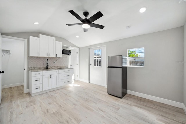 kitchen featuring lofted ceiling, decorative backsplash, freestanding refrigerator, white cabinets, and black microwave