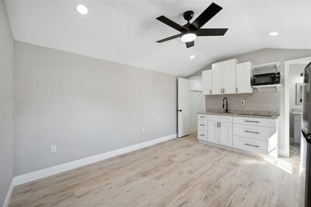 kitchen featuring lofted ceiling, a sink, light wood-style floors, decorative backsplash, and black appliances