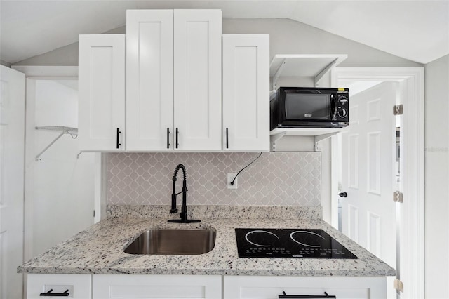 kitchen with vaulted ceiling, black appliances, a sink, and white cabinets