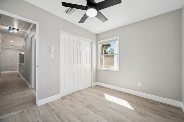 unfurnished bedroom featuring a closet, visible vents, attic access, wood finished floors, and baseboards