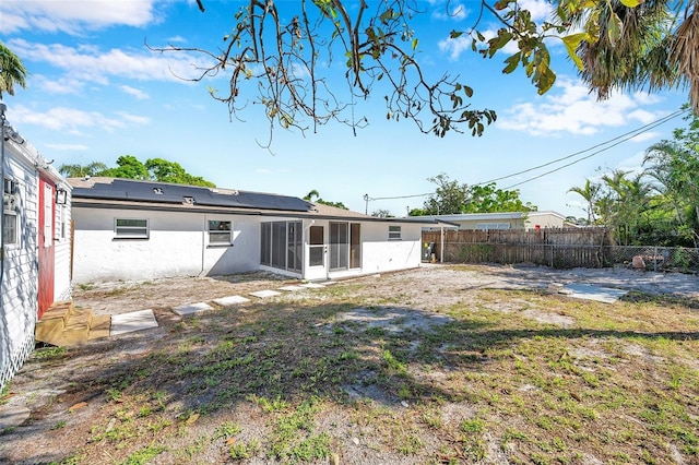 back of property with a sunroom, a fenced backyard, roof mounted solar panels, and stucco siding