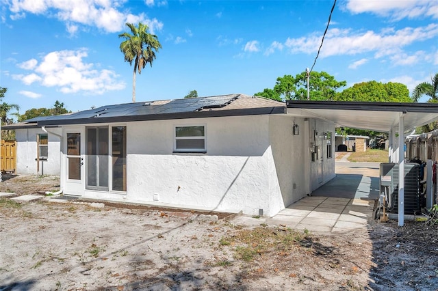 rear view of property featuring a carport, solar panels, central AC unit, and stucco siding