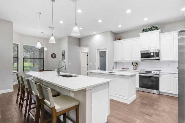 kitchen featuring decorative light fixtures, light countertops, appliances with stainless steel finishes, a kitchen island with sink, and a sink