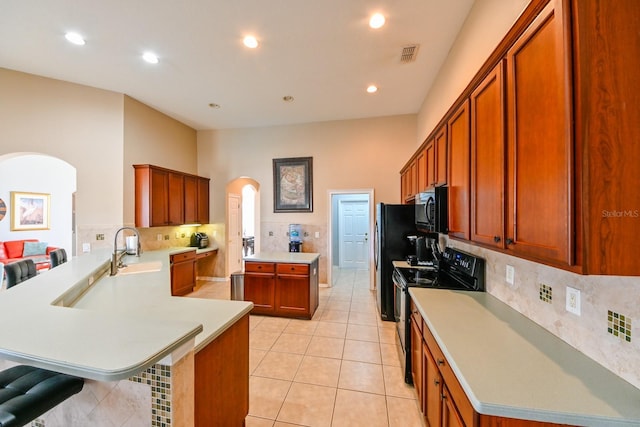 kitchen featuring light tile patterned flooring, a breakfast bar, kitchen peninsula, decorative backsplash, and black appliances