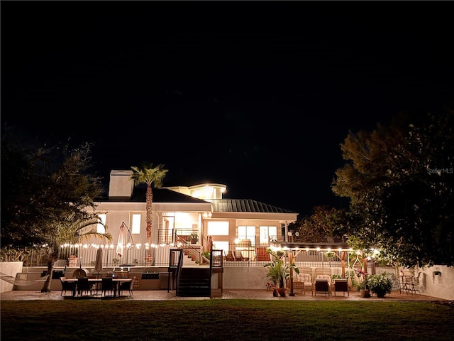 back of house at night featuring a patio, a lawn, and fence