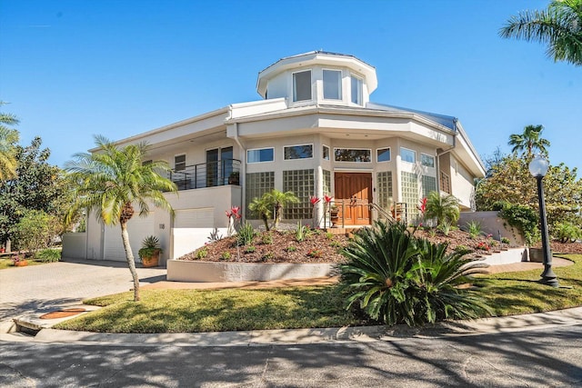 view of front of property featuring decorative driveway, an attached garage, a balcony, and stucco siding