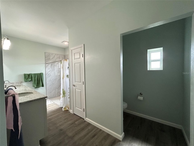 bathroom with toilet, vanity, tiled shower, and wood-type flooring