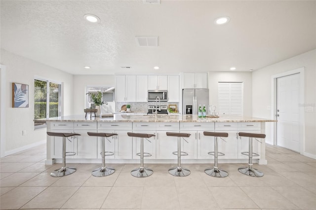 kitchen featuring appliances with stainless steel finishes, white cabinets, a large island, and a kitchen bar