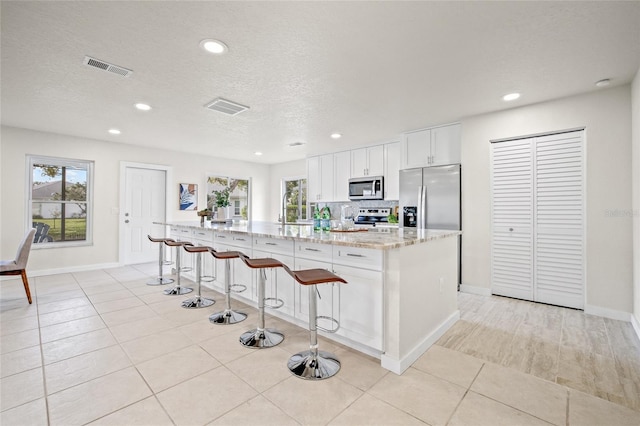 kitchen with a breakfast bar, visible vents, white cabinetry, appliances with stainless steel finishes, and an island with sink