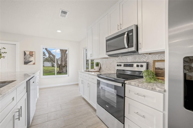 kitchen with stainless steel appliances, white cabinets, backsplash, and light stone countertops