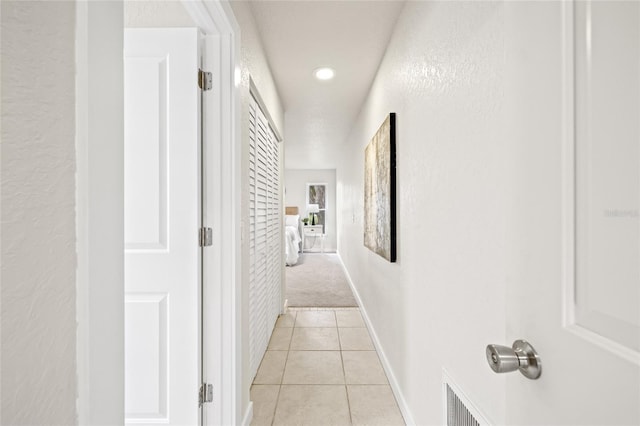 hallway with visible vents, a textured wall, baseboards, and light tile patterned floors