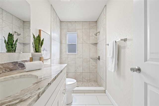 bathroom featuring a textured wall, toilet, vanity, tiled shower, and tile patterned floors