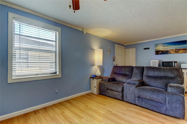 living room featuring ceiling fan, ornamental molding, light hardwood / wood-style floors, and a textured ceiling