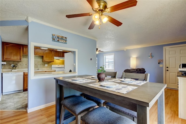 dining area featuring ceiling fan, ornamental molding, light wood-type flooring, and a textured ceiling