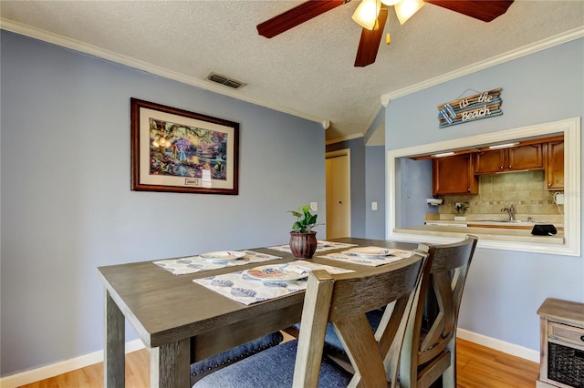 dining room with light wood-type flooring, crown molding, a textured ceiling, and ceiling fan