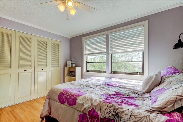 bedroom featuring light hardwood / wood-style floors, a closet, ceiling fan, a textured ceiling, and crown molding