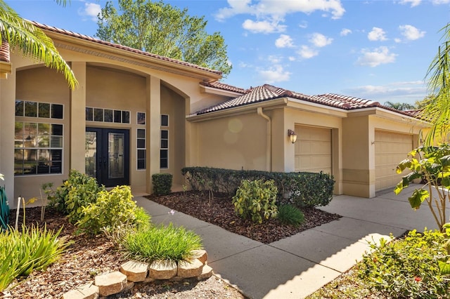 view of exterior entry with a tiled roof, a garage, driveway, and stucco siding