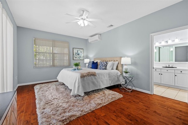 bedroom featuring visible vents, baseboards, light wood-type flooring, ensuite bath, and a wall mounted AC