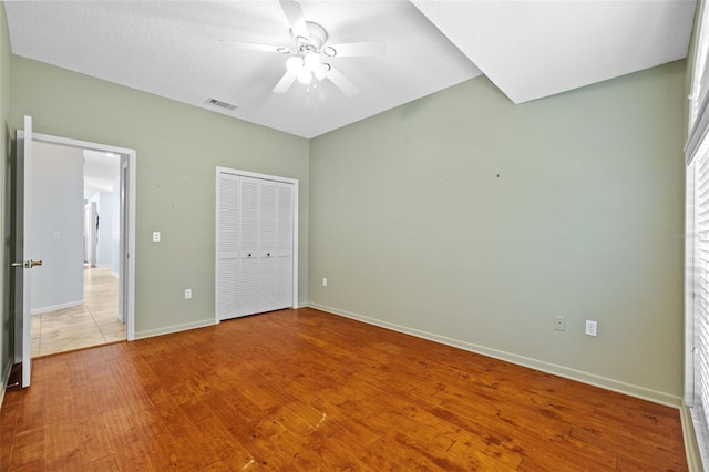 unfurnished bedroom with wood finished floors, visible vents, baseboards, ceiling fan, and a closet