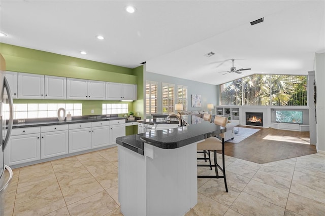 kitchen featuring a breakfast bar area, a ceiling fan, visible vents, white cabinets, and dark countertops