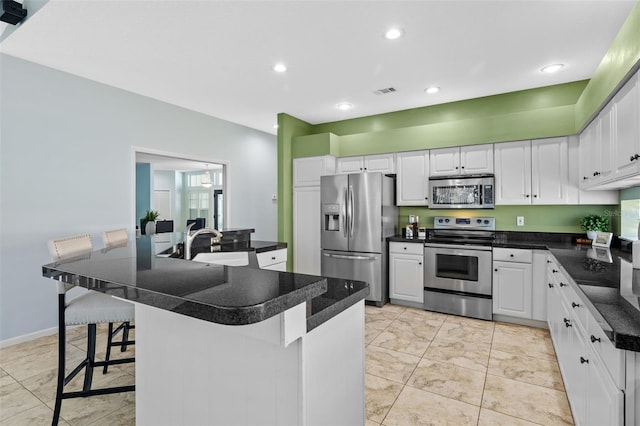 kitchen with a breakfast bar, a sink, dark countertops, appliances with stainless steel finishes, and white cabinets