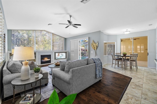 living area with visible vents, ceiling fan, vaulted ceiling, tile patterned floors, and a glass covered fireplace