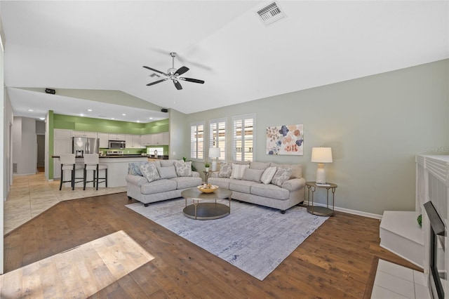 living area with a ceiling fan, baseboards, visible vents, vaulted ceiling, and light wood-type flooring