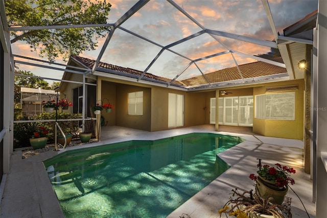 pool at dusk with glass enclosure, ceiling fan, and a patio area