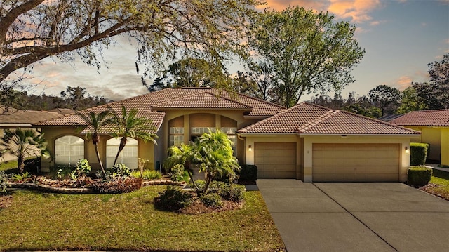 mediterranean / spanish home with driveway, a yard, stucco siding, a garage, and a tiled roof