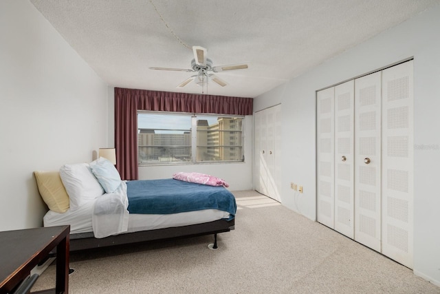 carpeted bedroom with ceiling fan, multiple closets, and a textured ceiling