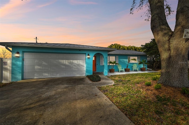 single story home with a garage, driveway, metal roof, a standing seam roof, and stucco siding