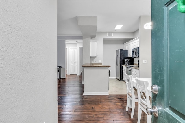 kitchen with baseboards, visible vents, hardwood / wood-style flooring, white cabinets, and appliances with stainless steel finishes