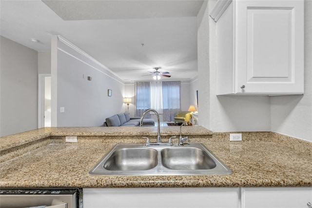 kitchen featuring open floor plan, light stone countertops, white cabinetry, and a sink