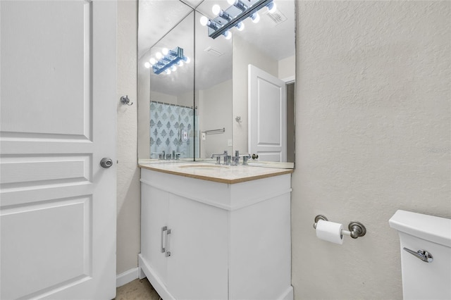 bathroom featuring toilet, vanity, and a textured wall