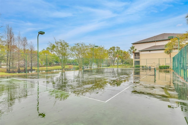 view of tennis court with fence and a water view