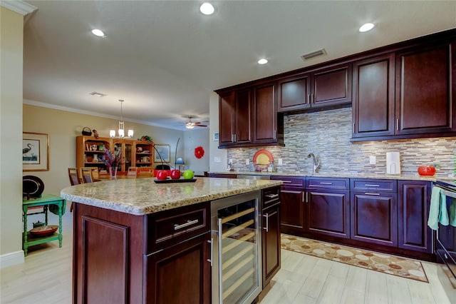 kitchen with visible vents, hanging light fixtures, decorative backsplash, a kitchen island, and beverage cooler