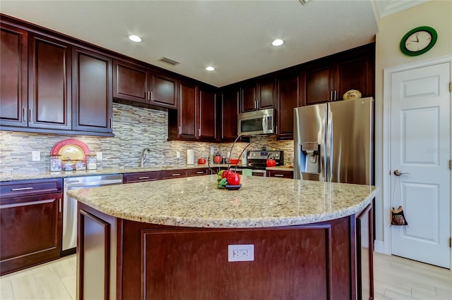 kitchen with a center island, visible vents, backsplash, appliances with stainless steel finishes, and light stone countertops