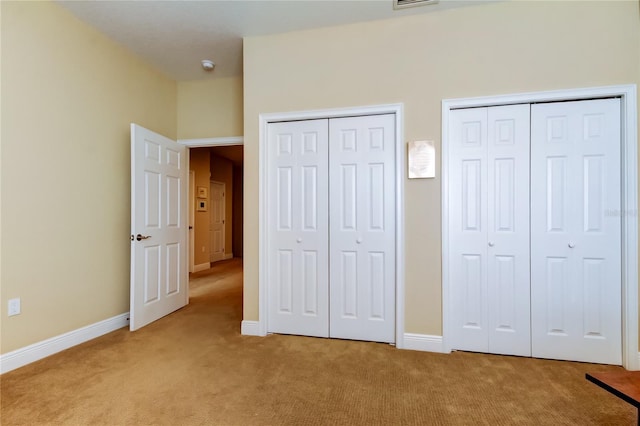 unfurnished bedroom featuring light carpet, baseboards, and two closets