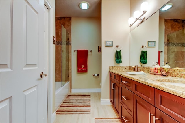 full bathroom with wood finished floors, a sink, baseboards, tiled shower / bath, and double vanity