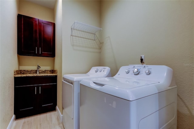 clothes washing area with cabinet space, baseboards, washer and dryer, light wood-style floors, and a sink