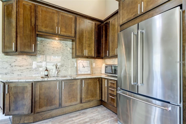 kitchen featuring light stone counters, light wood-style flooring, stainless steel appliances, a sink, and decorative backsplash